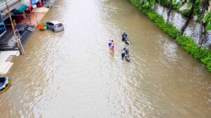 Climate Disaster - image : People with Motorcycles Crossing the Flooded Streets by Creativa Images