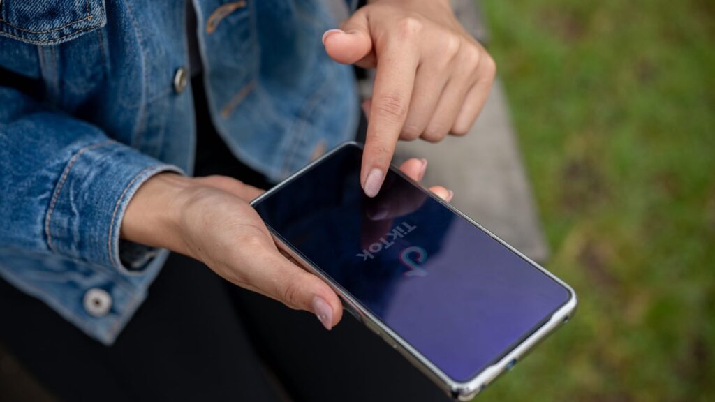 A close-up of a woman using the TikTok app on her smartphone while relaxing outdoors in a park by Bongkarngraphic from bongkarngraphic